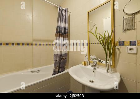 Salle de bains avec lavabo en porcelaine blanche avec pied assorti, miroir encadré de bois et baignoire avec rideau Banque D'Images