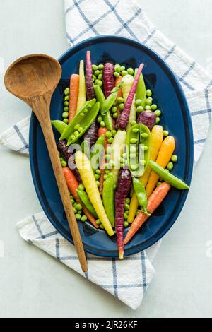 Un mélange de pois, de pois et de carottes arc-en-ciel sur une assiette ovale. Banque D'Images