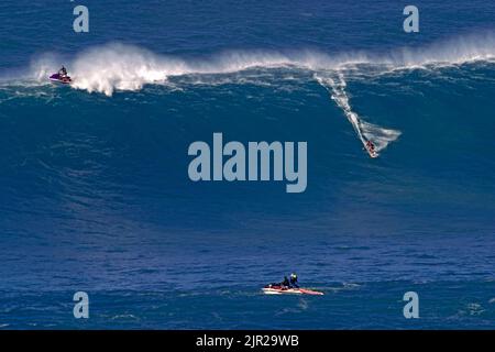 Un surfeur au remorquage tombe dans les grands vagues d'Hawaï à Peahi (Jaws) au large de Maui, tandis que son partenaire monte l'écusson sur le jetski qui a fait le remorquage. Banque D'Images