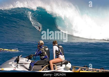 Un couple sur un jetski ont des sièges de première rangée à ce surfeur de remorquage tombant à la boucle de la grande vague de surf d'Hawaï à Peahi (Jaws) au large de Maui. Banque D'Images