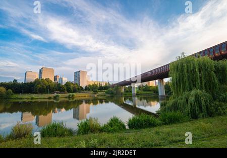 Vue panoramique sur un parc de la ville dans une banlieue de la ville de Prague avec le pont de métro Hůrka–Lužiny au-dessus d'un lac dans le parc. Banque D'Images
