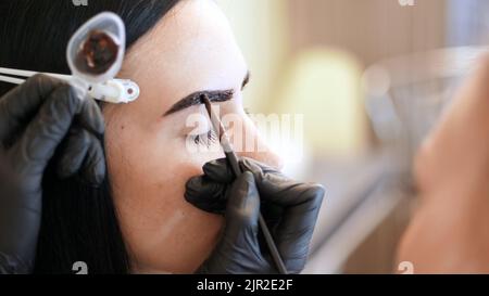 gros plan. jeune femme obtient la procédure de correction des sourcils. kosmetolog- maquilleuse applique la peinture avec brosse sur les sourcils dans le saloon de beauté. Soins professionnels pour le visage. Photo de haute qualité Banque D'Images