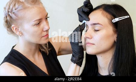 salon de beauté. le maître essuie la zone des sourcils avec un disque en coton humidifié avec un antiseptique. Photo de haute qualité Banque D'Images