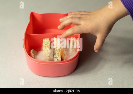 Une main d'enfant atteint pour un panier repas avec des tranches de pain et des saucisses sur lesquelles la moisissure blanche. Mauvaise nourriture gâtée dans la moisissure. Banque D'Images