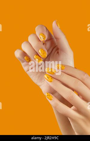 Des mains de femmes soignées avec un motif à ongles tendance sur fond orange Banque D'Images