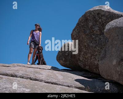 Vue horizontale d'une femelle trekker avec chocolat labrador retriever regardant la vue depuis un sommet de montagne. Banque D'Images