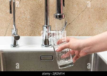 La main d'une femme tient un verre d'eau et le tire du robinet Banque D'Images