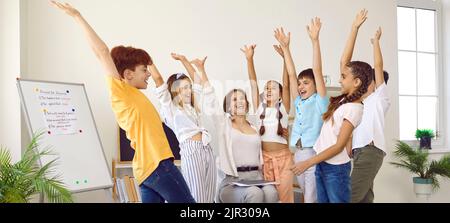 Groupe d'élèves de l'école primaire et leur enseignant levant les mains en sentant l'esprit d'unité. Banque D'Images