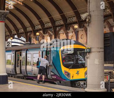 Un train se trouve à côté d'une plate-forme de gare, sous une voûte historique. La garde du train signale au conducteur de se mettre en marche. Banque D'Images