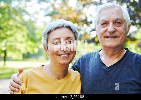 Un vieux couple optimiste et actif de 60s ans en amour pose à l'extérieur, sourire en regardant la caméra pendant une promenade matinale dans un parc public. Joyeux mariage sans fin, romantis Banque D'Images