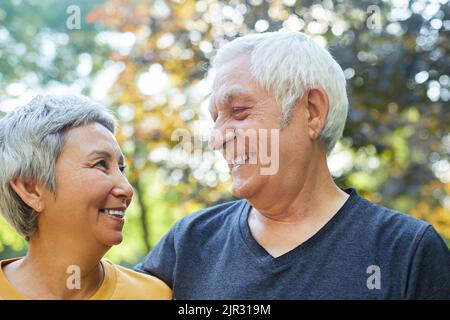 Optimiste attrayant multiracial 60s couple sportif pose dans le parc souriant regardant l'un l'autre avec tendresse et amour. Bonne nubile sans fin Banque D'Images