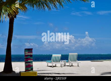 Une plage tranquille avec des chaises longues, du sable blanc, un palmier, de l'eau bleue, et un jeu de plage à Ambergris Caye, San Pedro, Belize. Banque D'Images