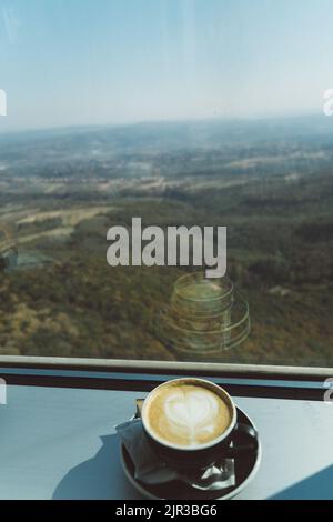 Une tasse de Cappuccino avec un motif de coeur sur une bordure de fenêtre avec une forêt en arrière-plan Banque D'Images
