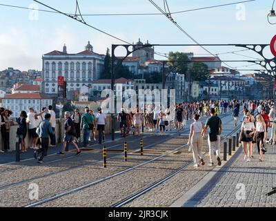 Pont Luis I à Porto, Portugal, avec des bâtiments derrière. Les gens marchent le long du pont qui est également utilisé par le métro, d'où les voies. Banque D'Images