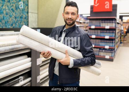 joli acheteur tenant une manne de rouleaux de papier peint dans un magasin de matériel Banque D'Images