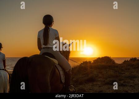 vue arrière de la jeune femme à cheval regardant le coucher du soleil. Banque D'Images