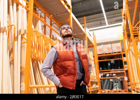 un homme dans un magasin de bois d'œuvre examine l'assortiment tout en regardant les racks avec des marchandises Banque D'Images