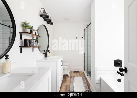 La salle de bains moderne de la ferme comprend un meuble-lavabo blanc et un comptoir en marbre, des miroirs circulaires noirs et une vue sur la douche carrelée de métro blanche. Banque D'Images