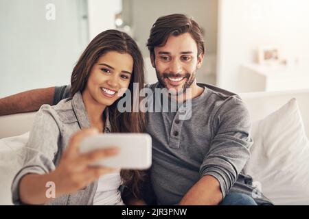 Le sourire parfait pour un selfie rapide. Un jeune couple attrayant passant du temps de qualité à la maison. Banque D'Images