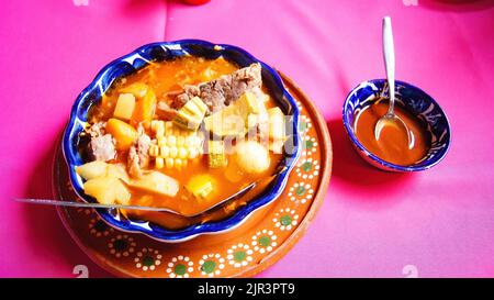 Assiette en argile avec pozole, cuisine mexicaine traditionnelle, nappe rose, cuillère en métal Banque D'Images