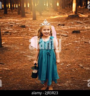 Je suis une véritable fée de la vie. Une petite fille heureuse regardant l'appareil photo et tenant une lampe tout en se tenant à l'extérieur dans les bois. Banque D'Images