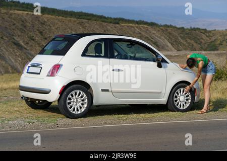 La jeune femme s'occupe de vérifier les jantes de la roue contre les pentes en campagne par beau temps Banque D'Images