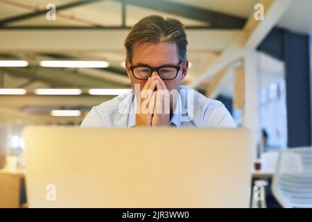 La saison des sniffle refrappe. Un homme d'affaires éternuant tout en utilisant son ordinateur portable au bureau. Banque D'Images