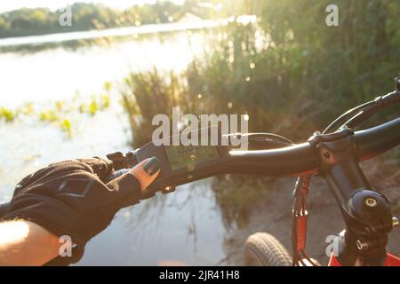 une main femelle dans un gant noir tient le volant d'un e-bike au soleil dans le parc, conduisant un e-bike, se reposant sur un vélo Banque D'Images