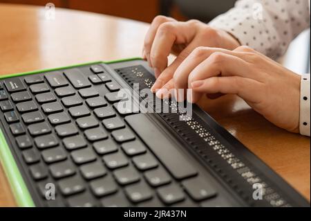 Une femme aveugle utilise un ordinateur avec un écran en braille et un clavier d'ordinateur. Périphérique inclus. Banque D'Images