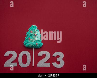 2023 et des bonbons bleus sous forme d'arbre de Noël sur fond rouge Banque D'Images