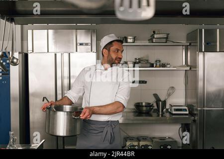 Chef cuisant un plat savoureux dans la cuisine du restaurant en utilisant l'équipement moderne Banque D'Images