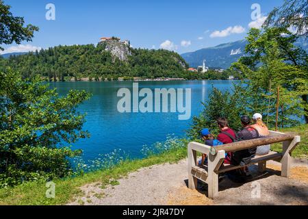 Bled, Slovénie - 18 juillet 2022 : famille de quatre personnes Profitez d'une vue panoramique sur le lac de Bled et le château de Bled depuis un banc, destination touristique populaire. Banque D'Images