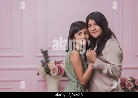 Une mère hispanique avec sa fille embrassant sur un fond rose Banque D'Images