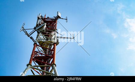 Mât de communication rouge et blanc avec antennes contre ciel bleu Banque D'Images