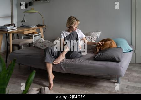 Triste femme d'âge moyen inquiète assise sur un canapé prenant soin de vieux animaux malades à la maison, dépression chez les chiens Banque D'Images