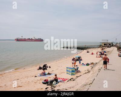 Un grand cargo passe devant la plage d'été et les touristes sur la côte de l'île Canvey, l'estuaire de la Tamise, Essex, Angleterre, Royaume-Uni Banque D'Images