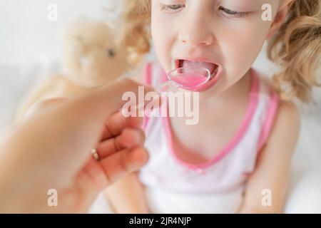 L'enfant boit du sirop à l'aide d'une cuillère de mesure. Banque D'Images