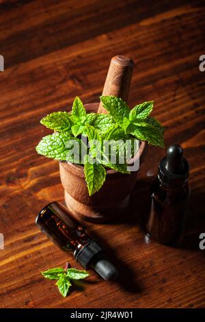 Feuilles d'herbes de menthe fraîche poivrée dans le mortier et huile essentielle dans les flacons compte-gouttes Banque D'Images