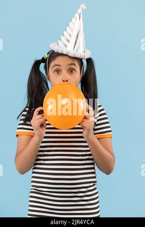 Petite fille soufflant ballon jaune sur fond bleu Banque D'Images