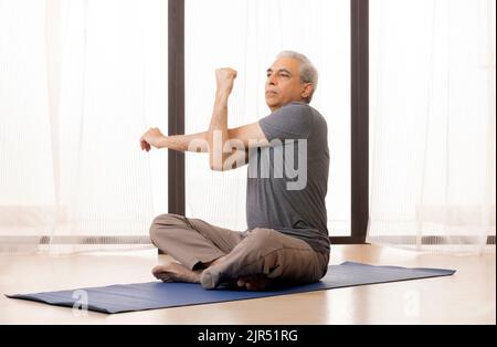 Portrait d'un homme senior actif faisant un exercice d'étirement à la maison Banque D'Images