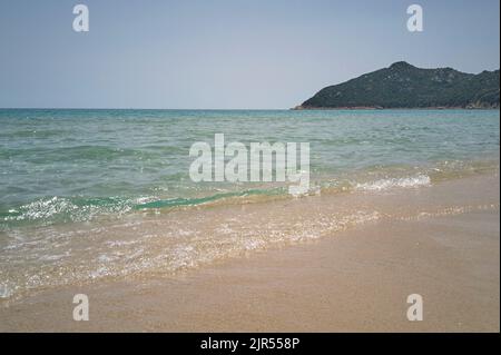 La mer cristalline avec des vagues se brisant sur le sable de la plage immergée dans un paysage typique du sud de la Sardaigne. Banque D'Images