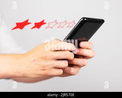 Mains tenant le téléphone pour donner deux étoiles de rétroaction. Enquête de satisfaction. Expérience client négative. Femme utilisant un smartphone pour l'évaluation du service, de l'hôtel, de l'application et du restaurant. Photo de haute qualité Banque D'Images