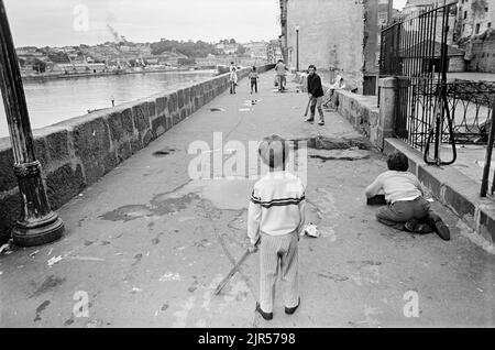 PORTUGAL - PORTO - 1970. Les enfants jouent à la chauve-souris et au ballon sur le front de mer de Cais da Estiva, sur le fleuve Douro, dans le quartier de Ribeira à Porto, dans le nord du pays Banque D'Images