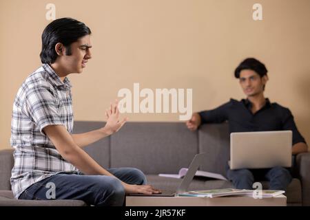 Deux adolescents heureux faisant leurs devoirs à la maison à l'aide d'un ordinateur portable Banque D'Images