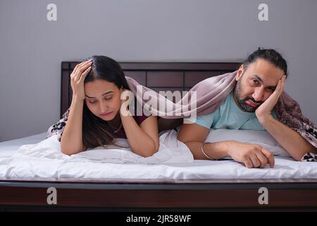 Couple fatigué allongé ensemble sous une couverture sur le lit Banque D'Images