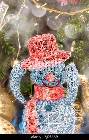 Une figurine bonhomme de neige dans un chapeau et un foulard faits de guirlandes et de guirlandes fait son salut. Félicitations pour la nouvelle année 2023. Décoration de Noël Banque D'Images