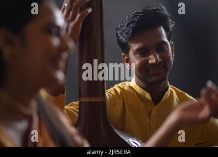 Vue rapprochée d'un jeune musicien masculin accompagnant une musicienne sur Tanpura pendant la représentation en scène Banque D'Images