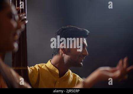 Vue rapprochée d'un jeune musicien masculin accompagnant une musicienne sur Tanpura pendant la représentation en scène Banque D'Images