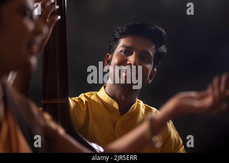 Vue rapprochée d'un jeune musicien masculin accompagnant une musicienne sur Tanpura pendant la représentation en scène Banque D'Images