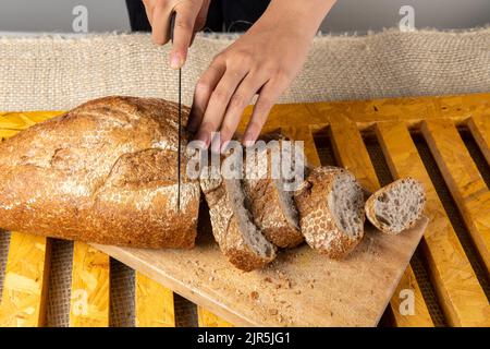 les mains de la femme trancheuse le pain de levain complet sur une table en bois Banque D'Images